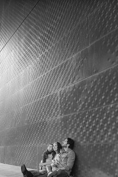 three people sitting on the ground next to a wall