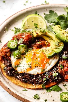 an egg is on top of some black beans and avocado as it sits on a tortilla