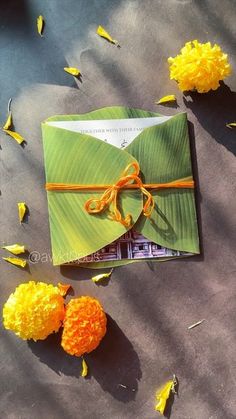 an open book with yellow and orange flowers on the ground next to it, surrounded by petals