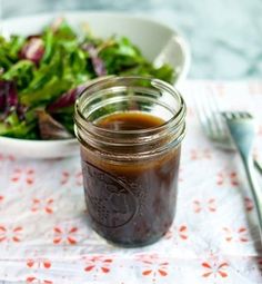 a salad with dressing in a jar next to a fork and spoon on a table