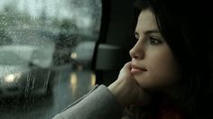 a woman sitting in the passenger seat of a car with rain falling down on her