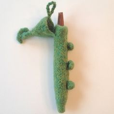 a green crocheted alligator ornament hanging from a hook on a white wall