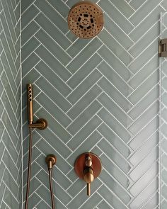 a bathroom with herringbone tile on the wall and shower head, hand held by brass faucets