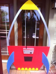 a cardboard rocket ship sitting on top of a wooden table in front of a door