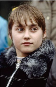 a young boy wearing a black jacket with a fur collar around his neck looking at the camera