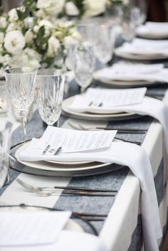 the table is set with place settings, silverware and white flowers in vases