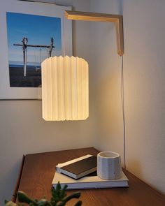 a table lamp sitting on top of a wooden table next to a cup and book