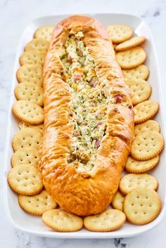 a white platter filled with crackers and a long sandwich on top of it