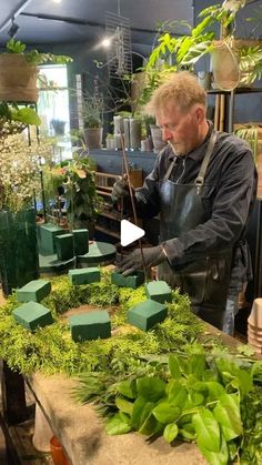 a man working in a flower shop with lots of plants and greenery on display