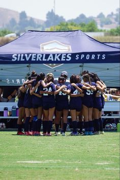 a group of girls soccer players huddle together in front of a tent on the field