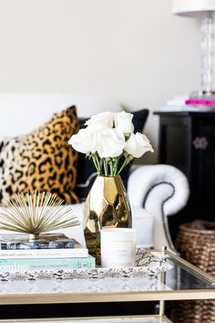 white roses in a gold vase on a coffee table with books and leopard print pillows