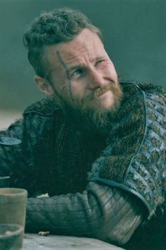 a man with a beard sitting at a table in front of a cup and looking off to the side