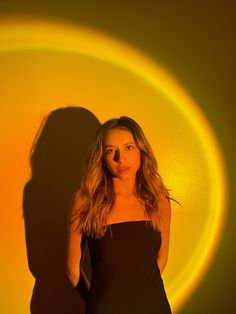 a woman standing in front of a yellow circle with her shadow on the wall behind her