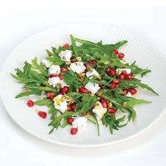 a white plate topped with greens and pomegranate