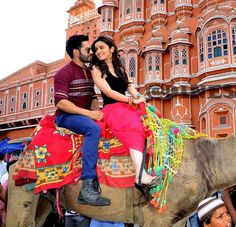 a man and woman riding on the back of an elephant in front of a building