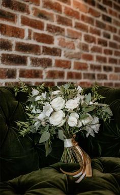 a bouquet of white flowers sitting on top of a green velvet couch next to a brick wall