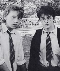 two young men standing next to each other in front of a stone wall and trees