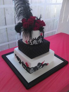 three tiered cake with black and white designs on top, decorated with red roses