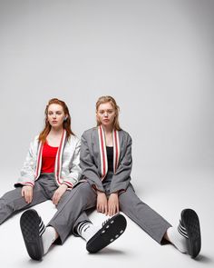 two young women sitting on the ground with their feet crossed and one wearing headphones