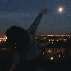 a person reaching up in the air to catch a frisbee at night time