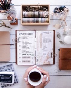 a person holding a cup of coffee in front of an open book on top of a table