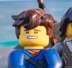 two lego men standing next to each other near the ocean