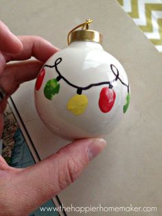 a hand holding a white ornament with christmas lights on it's side