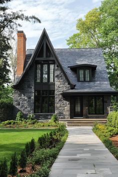 a house with black shingles and stone walkway leading to the front door, surrounded by greenery