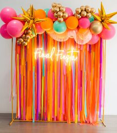 an orange, pink, and yellow backdrop with streamers and balloons that say final fiesta