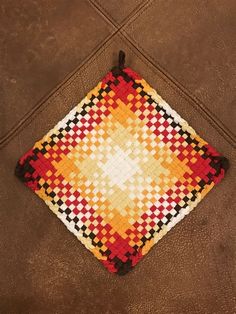 a square shaped cushion made out of woven material with an orange, yellow and red pattern