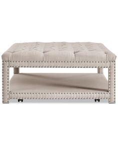 a white bench with studded legs and a beige cushion on the bottom, sitting in front of a white background