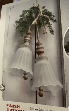 two white bells hanging from the side of a wooden door with pine cones and twine