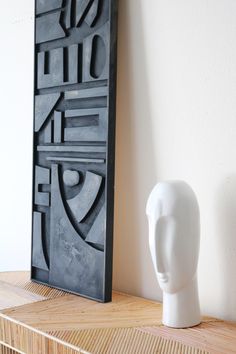 a white vase sitting on top of a wooden shelf next to a black framed art piece