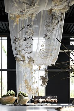 an open room with sheer curtains and flowers in vases on the floor next to windows