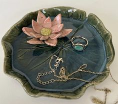 a green plate with a flower on it next to two rings and a chain necklace