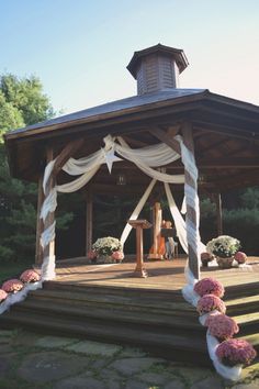 the gazebo is decorated with white drapes and pink flowers on the steps leading up to it