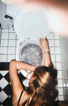 a woman standing in front of a toilet with her hands on the seat and looking down