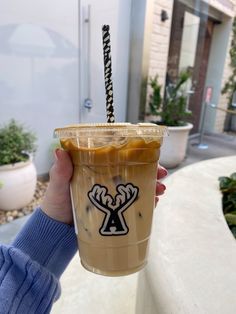 a person holding up a drink in front of a building with an ant logo on it