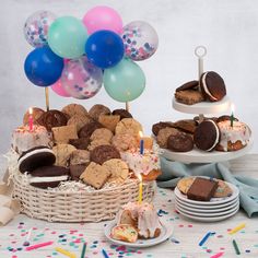 a table topped with lots of desserts and balloons next to plates filled with cake