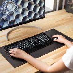 a woman using a computer keyboard and mouse on a wooden desk in front of a monitor