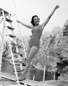 a woman in a bathing suit jumping off a ladder into the water with her arms outstretched