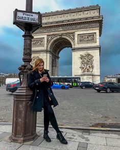 a woman leaning against a pole in front of the arc de trioe