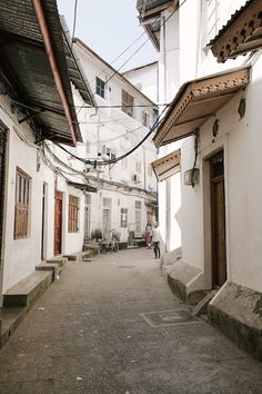 two people are walking down an alleyway in the old part of town with white buildings