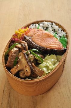 a wooden bowl filled with meat, rice and veggies on top of a table