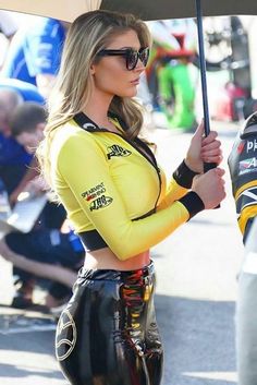 a woman in yellow shirt and black pants holding an umbrella with her hands behind her back