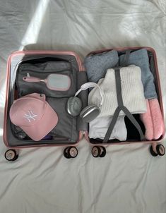 an open suitcase with clothes and accessories inside on a bed sheeted surface in front of a white background