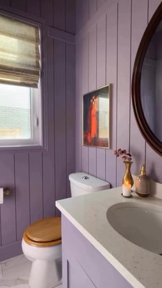 a white toilet sitting next to a sink in a bathroom under a window with purple walls