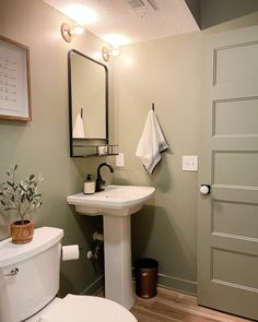 a white toilet sitting next to a sink in a bathroom under a mirror and lights