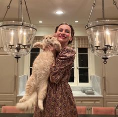 a woman holding a cat in her arms while standing next to two chandeliers