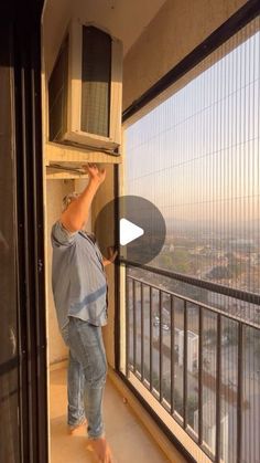 a man standing on top of a window sill next to a metal rail and air conditioner